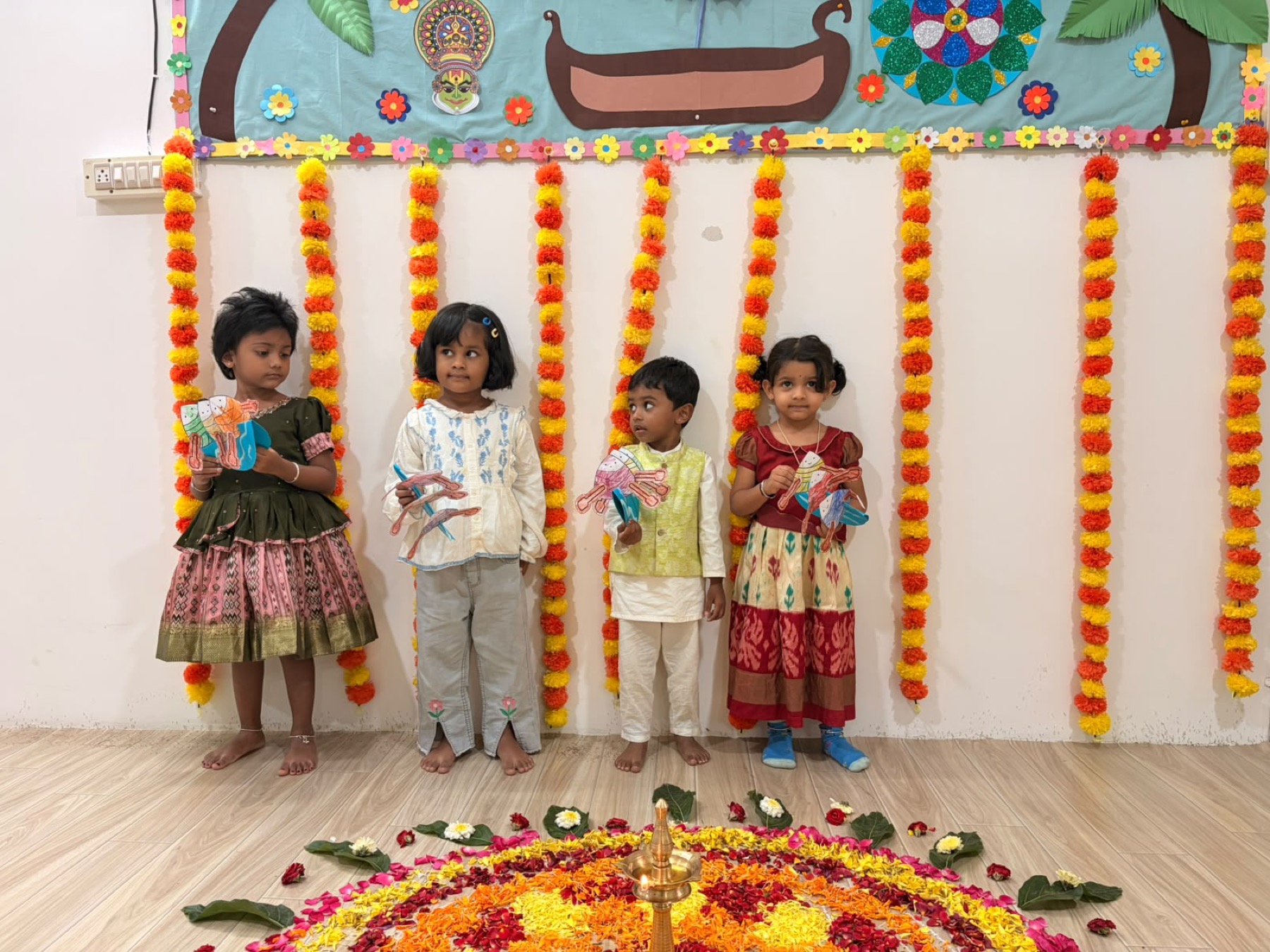 Children standing beside a flower rangoli during an Onam celebration at Tender Moments Hebbal